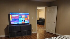 Ein Schlafzimmer mit einem Bett, einem Fernseher auf einem Schrank, einem Deckenventilator und einer Tür zu einem anderen Raum.