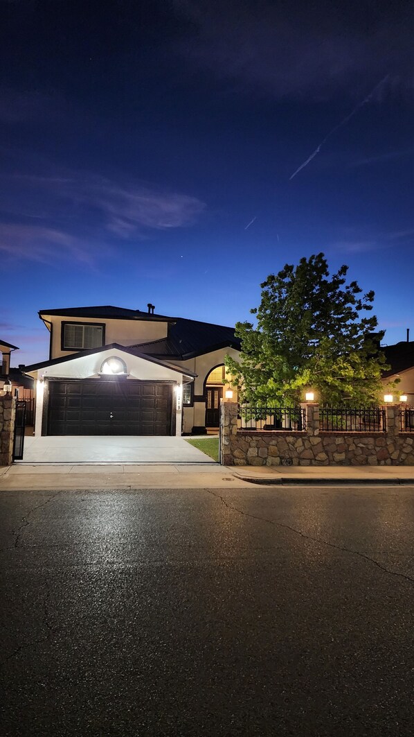 A two-story house with a garage, stone wall, and a tree in front.