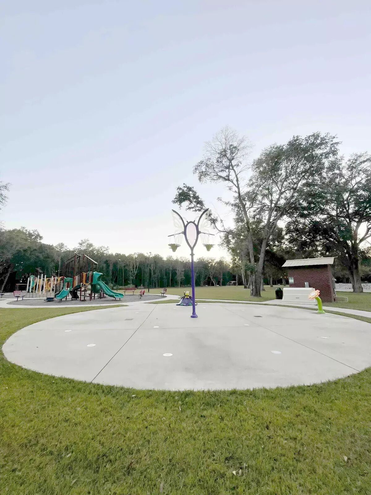 Un parc avec une aire de jeux, un lampadaire violet et une pelouse.