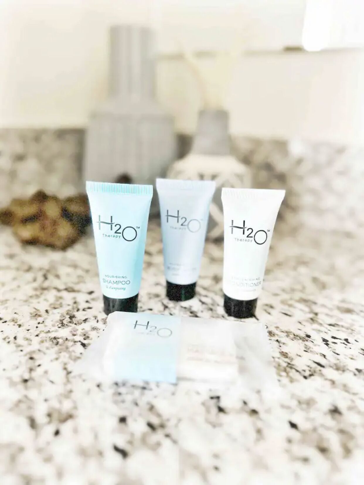 Three H2O Therapy shampoo tubes on a granite countertop.