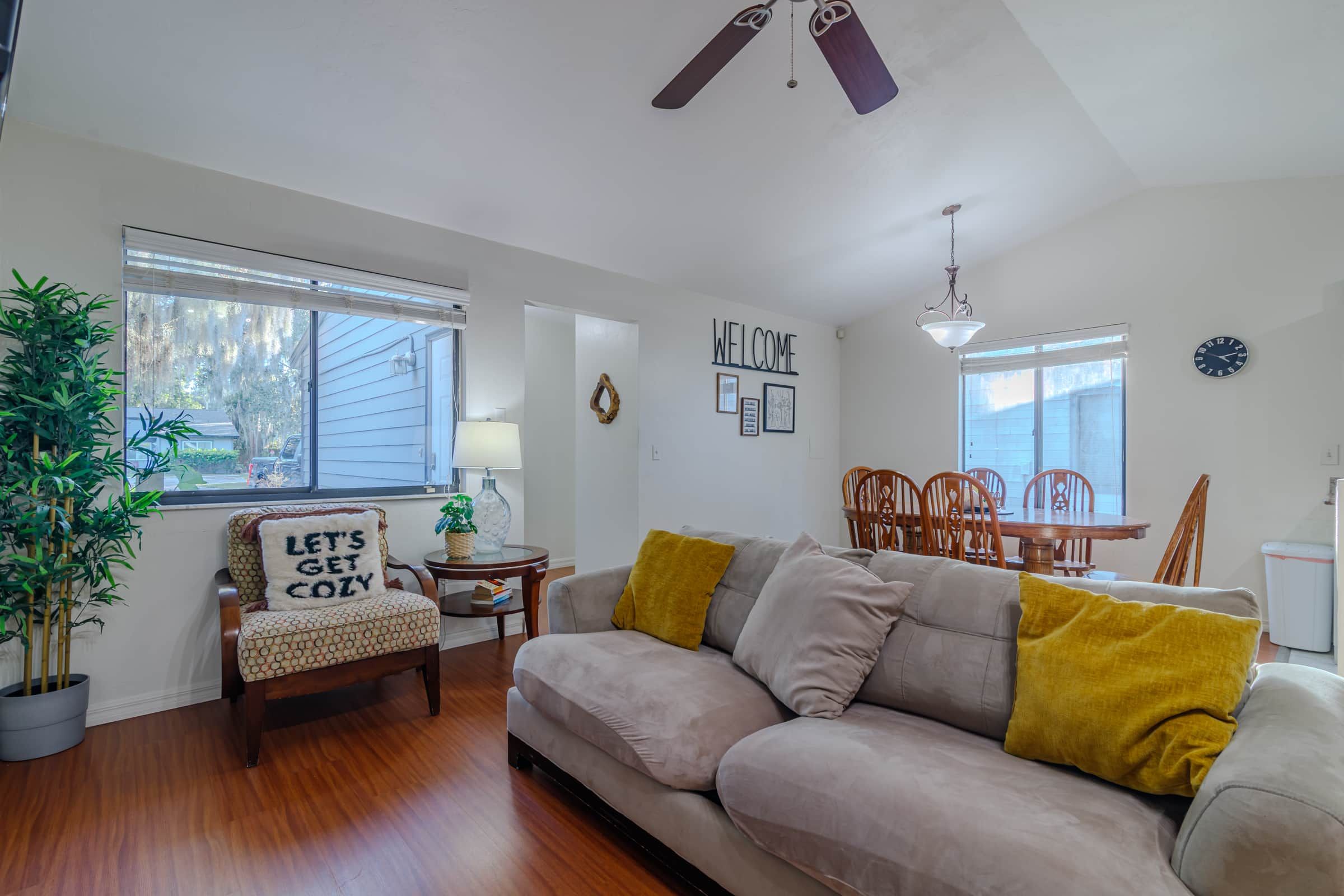A living room with a sofa, a chair, a dining table, and a ceiling fan.