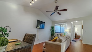 Una sala de estar moderna con televisor de pantalla plana, ventilador de techo, mesa de comedor con sillas y sofá.