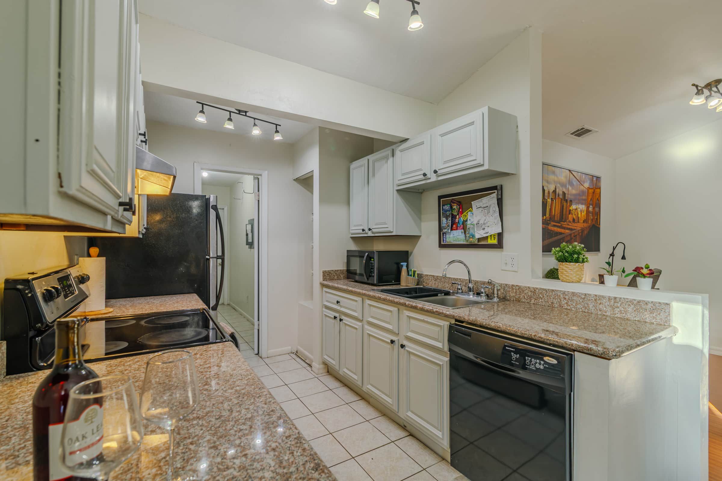 A modern kitchen with white cabinets, a granite countertop, a dishwasher, and a microwave.