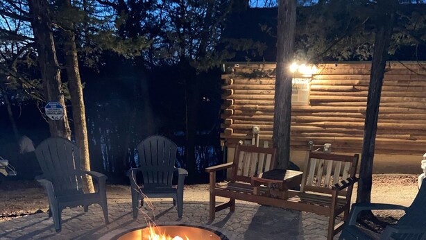 Ein Lagerfeuer, umringt von Holzstühlen und einer terrasse mit Steinbelag.