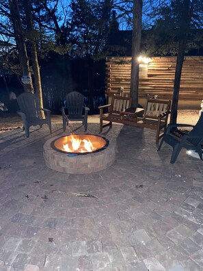 A fire pit surrounded by wooden chairs and a stone-paved patio.
