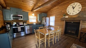 Eine Kücheneinrichtung in einer Blockhütte mit Holzschränken, einem Esstisch mit Stühlen, einer Uhr und einem Kamin.