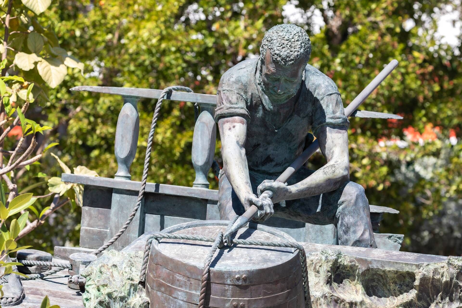 A statue of a person working with a tool, surrounded by a rope and a barrel.