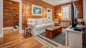 A living room with a wooden wall, a white sofa, a wooden coffee table, and a ceiling fan.