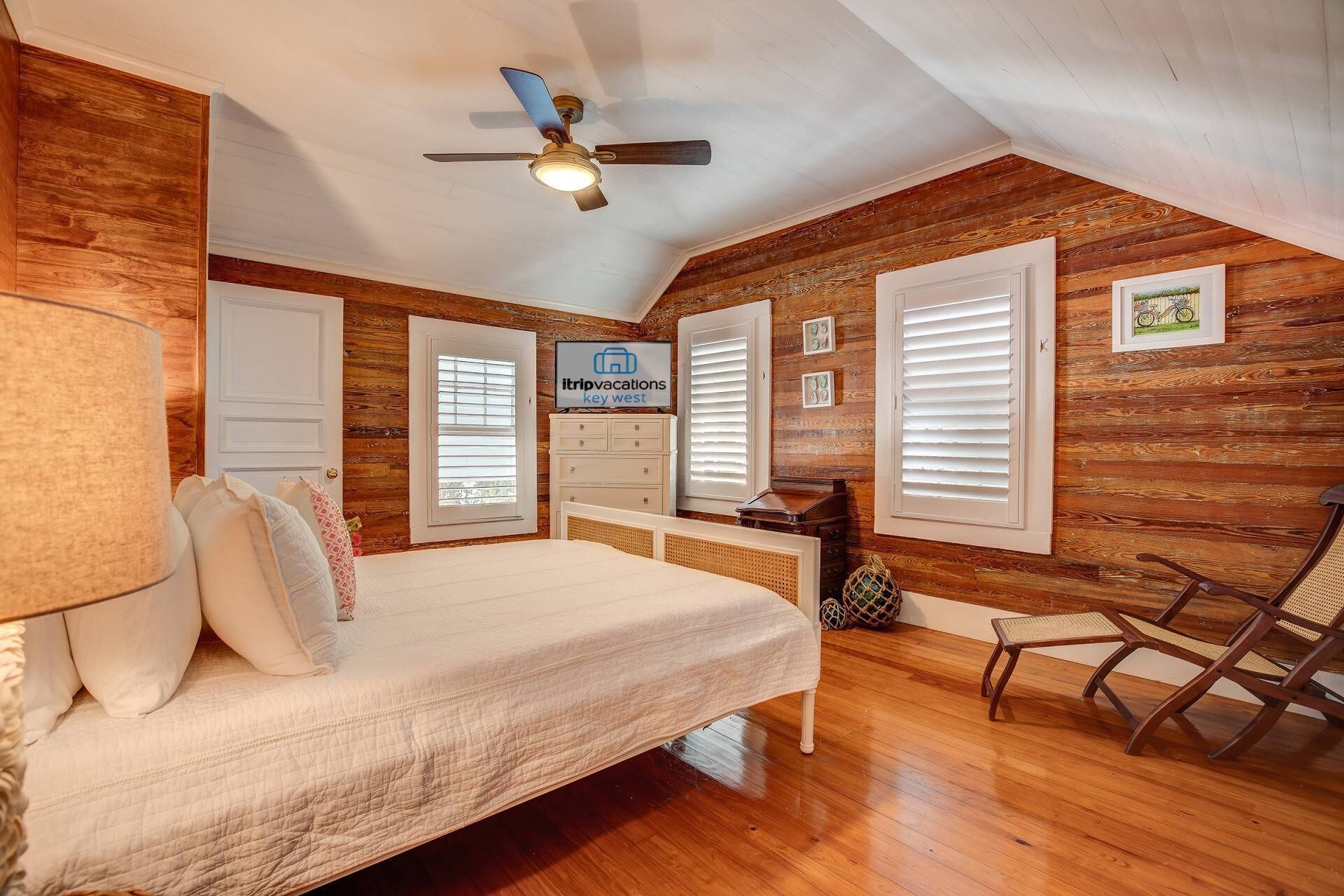Un dormitorio acogedor con cama, ventilador de techo, paredes de madera y un letrero que dice 'itripvacations key west'.