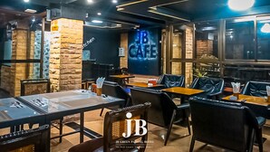 Un restaurante con una decoración moderna, que presenta paredes de piedra, sillas de cuero negro y mesas con tapas de vidrio.