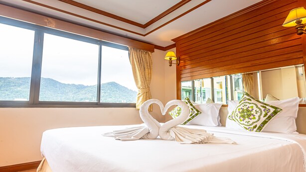 Una habitación de hotel con una cama grande, una toalla dispuesta en forma de corazón y vistas a las montañas a través de la ventana.