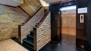 Una escalera con barandillas de madera y paredes de piedra, un ascensor y un cartel que indica 'Piso 6'.