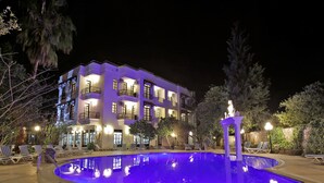 Un hôtel à plusieurs étages doté d’une piscine, de chaises longues extérieures et d’une façade bien éclairée.