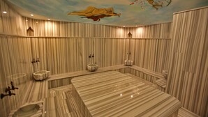 Une salle de spa dotée d’une grande baignoire en marbre, de murs à rayures et d’une fresque représentant une femme peinte au plafond.