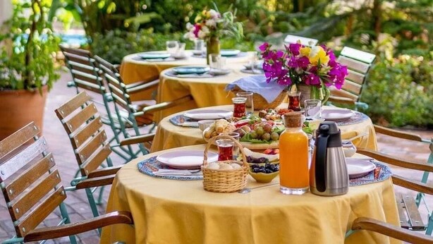 Un espace extérieur aménagé pour les repas, avec des tables rondes recouvertes de nappes jaunes, entourées de chaises en bois.