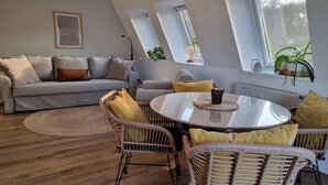 A modern living room with a grey sofa, wicker chairs, a round table, and skylights.