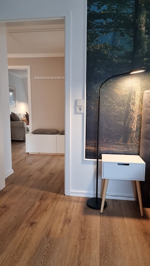 Une pièce moderne avec un plancher en bois, un canapé blanc, une petite table blanche et un lampadaire.