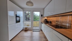 A modern kitchen with white cabinets, a wooden countertop, and a view of the outdoors through a glass door.