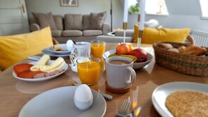 A breakfast table with plates of food, glasses of orange juice, a coffee mug, and a basket of bread.