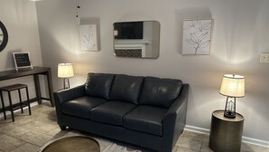 A modern living room with a dark leather sofa, two standing lamps, a round coffee table, and a small side table. - Quiet and Cozy Home in the Heart of Southaven (Southaven)