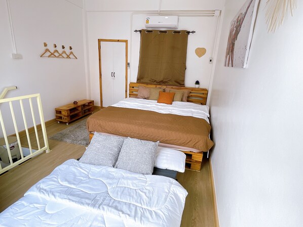 Quarto com cama, cabeceira de madeira, pequena mesa de cabeceira, ar condicionado fixado na parede, porta e prateleira na parede com uma planta.