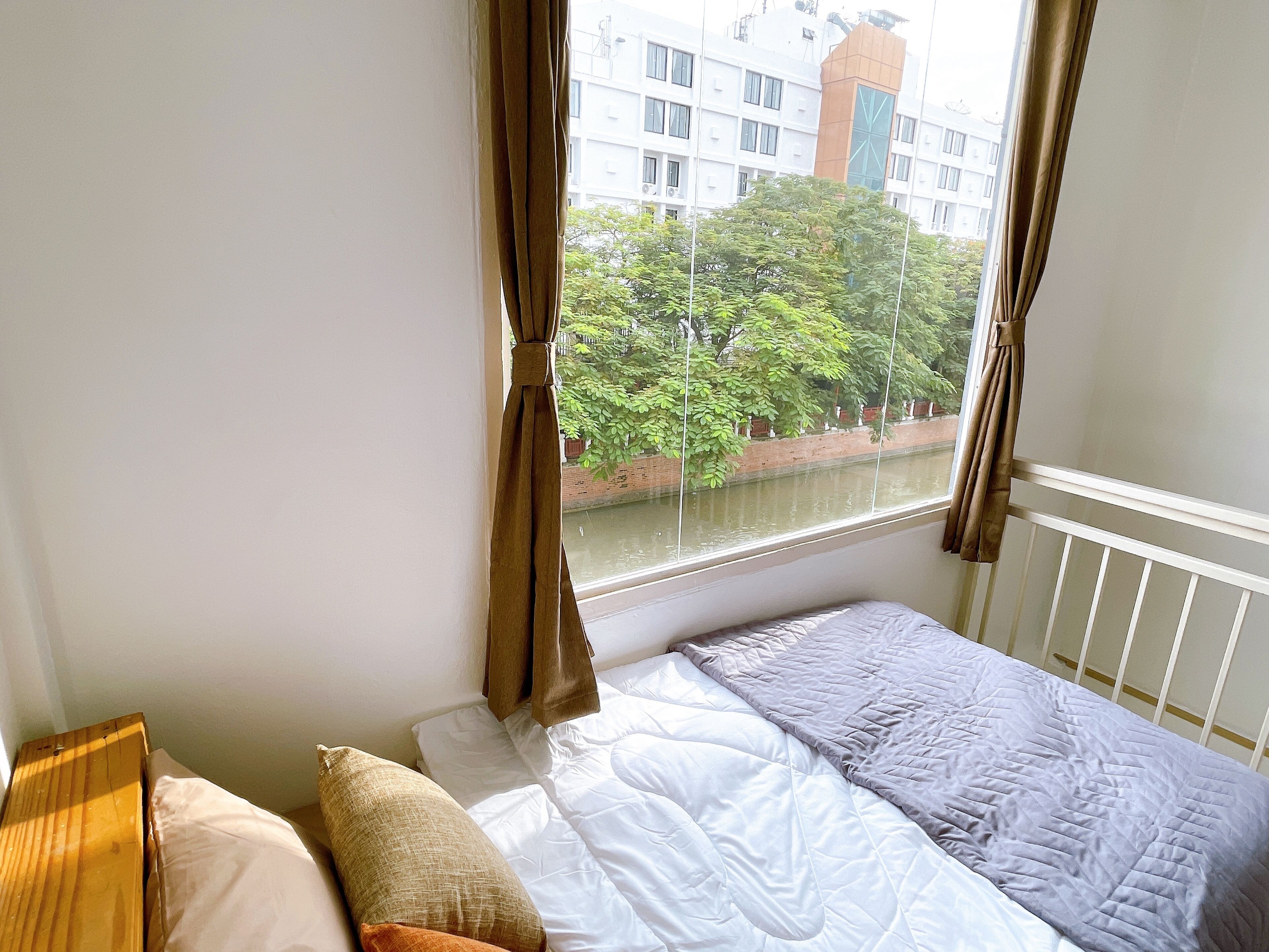 Un dormitorio con cama, cortinas y vista a un edificio y árboles a través de una ventana.