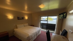A hotel room with a bed, a desk, a chair, a window with a view of the sea, and a ceiling light. - Lakes Lodge Okataina (Lake Okataina)