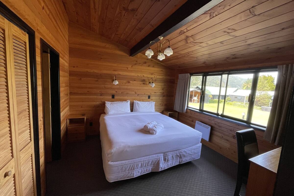 Une pièce en bois avec un grand lit, une petite table et une fenêtre donnant sur l’extérieur.