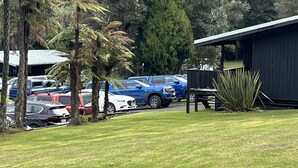 A parking area with several cars, a building, and a grassy field with trees. - Lakes Lodge Okataina (Lake Okataina)