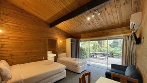 A cabin with wooden walls, a large window, a bed, a sofa, and a table. - Lakes Lodge Okataina (Lake Okataina)