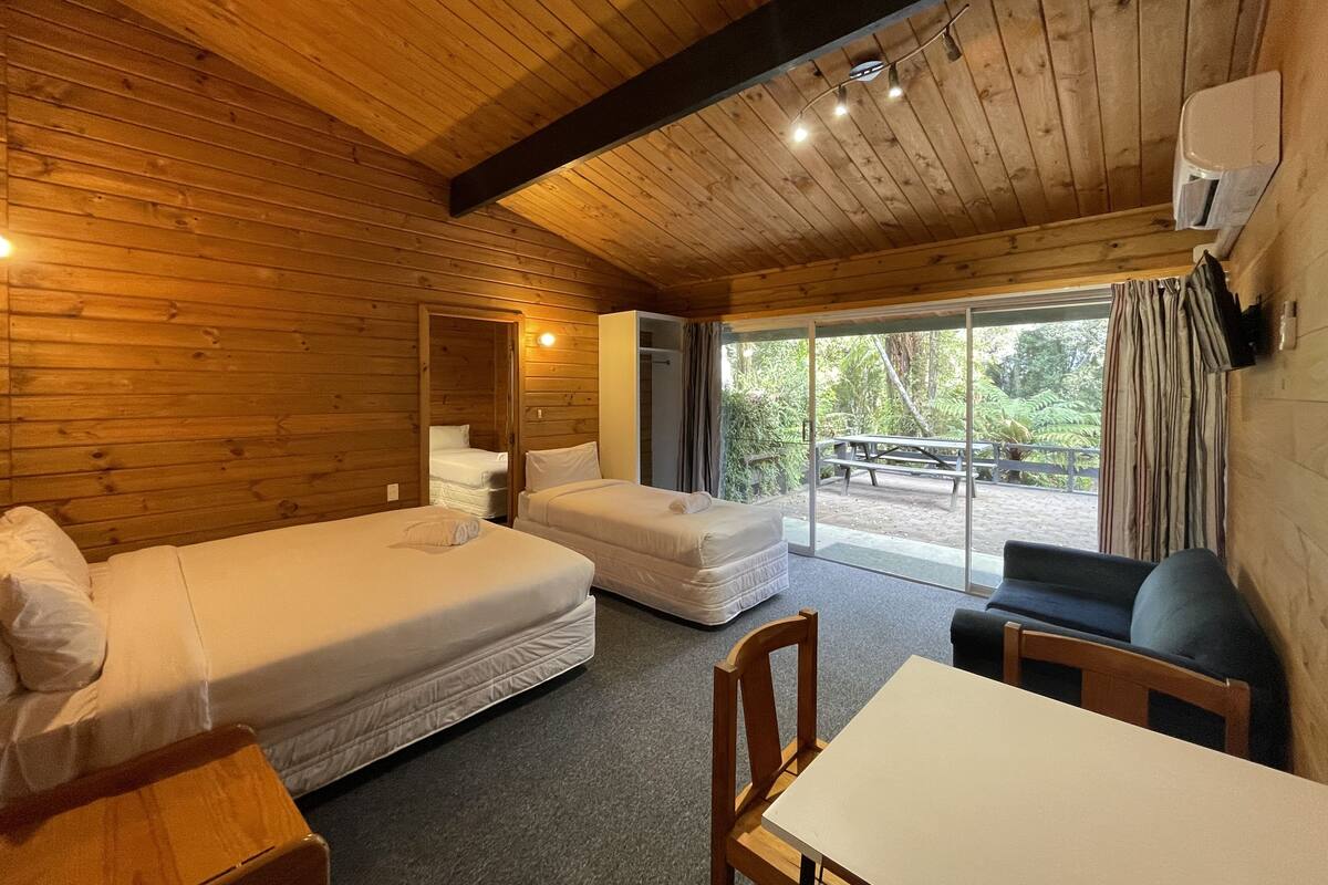 Une cabane aux murs en bois, avec une grande fenêtre, un lit, un canapé et une table.