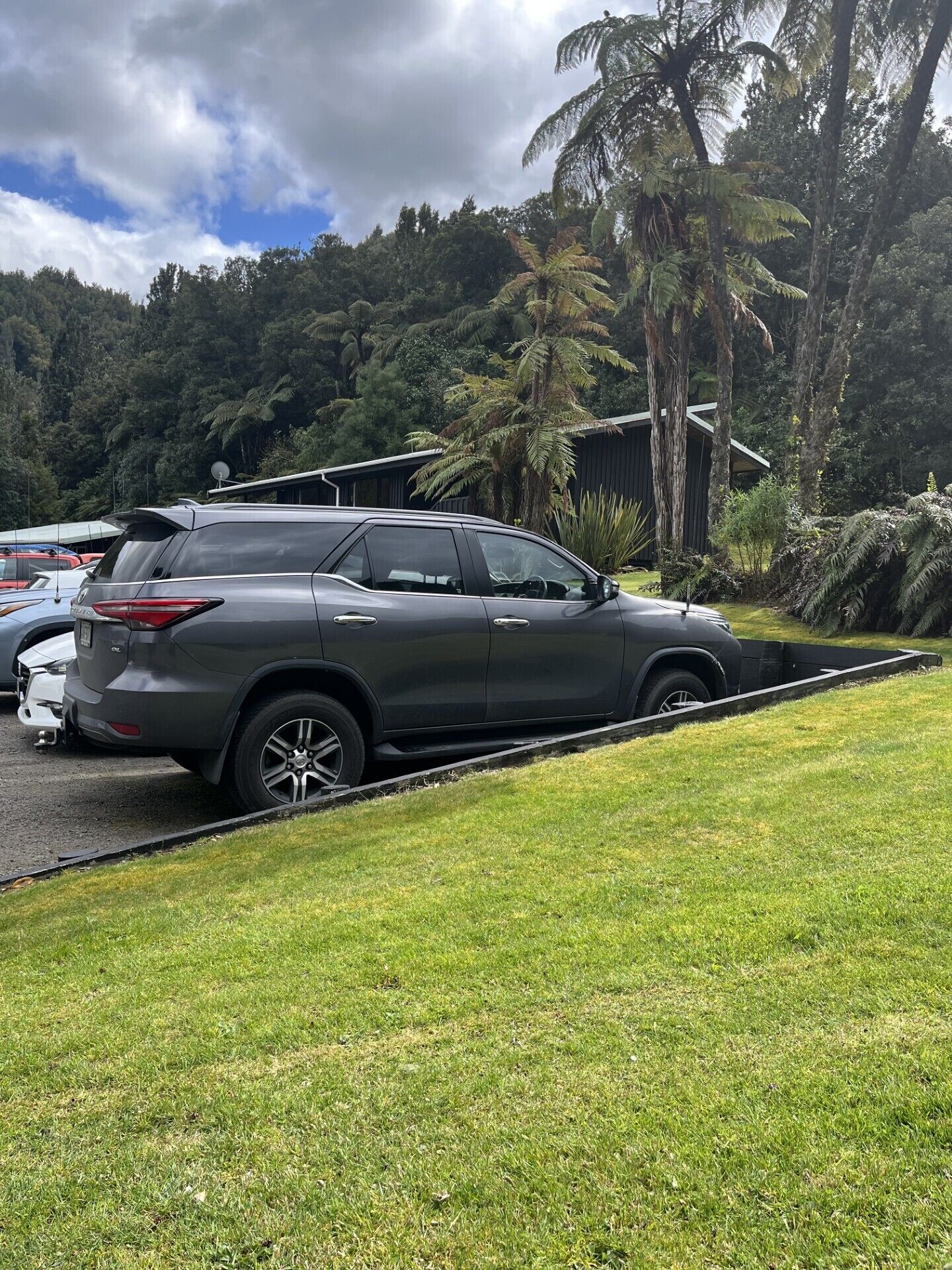 A parking area with a dark-colored SUV parked on a grassy slope.