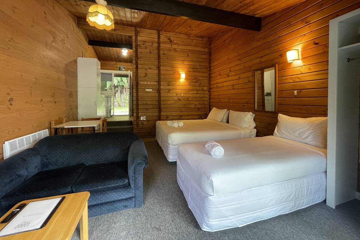 Une pièce aménagée comme un chalet en bois, avec deux lits, un canapé, une table avec un menu et un petit coin cuisine.