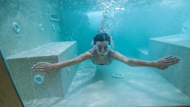Ein Blick unter Wasser auf einen Swimmingpool mit klarem Wasser, erkennbaren Beckenrändern und einem gefliesten Boden.