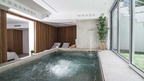Ein moderner Poolbereich im Innenbereich mit Spa-Bereich, Holzvertäfelung und Blick nach außen.