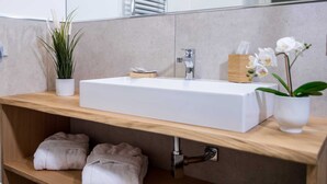 Ein modernes Badezimmer mit einem großen weißen Waschbecken, einem Holzschrank, einer Topfpflanze und einem Spiegel.