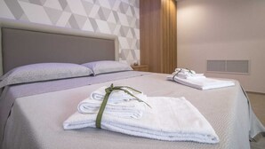 Ein modernes Hotelzimmer mit einem großen Bett, Wänden in Grau und Weiß mit Muster, einer Holzpaneel-Akzentwand und ordentlich gefalteten Handtüchern auf dem Bett.