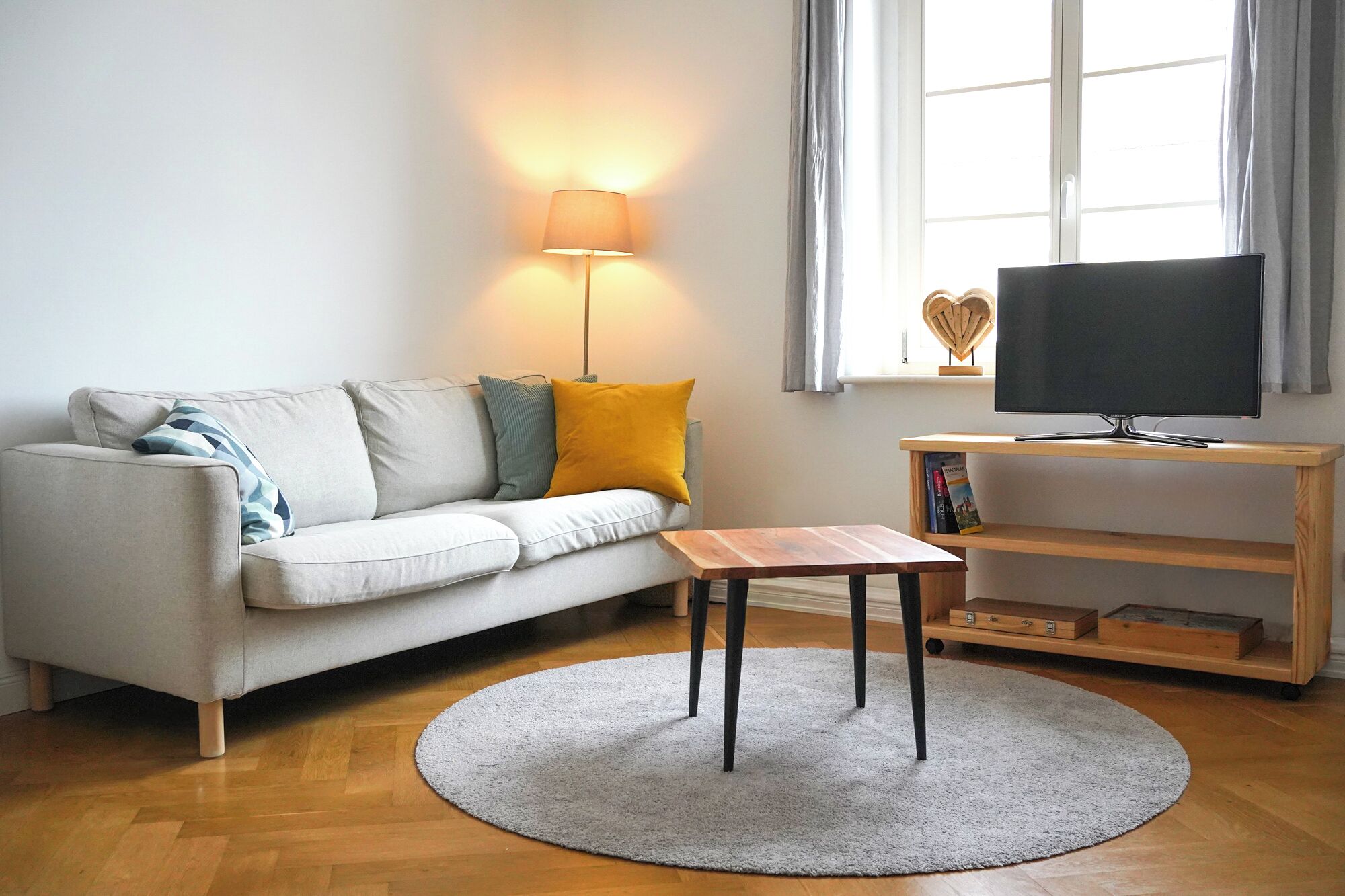 A living room with a sofa, a small wooden table, a TV on a wooden stand, and a round rug.