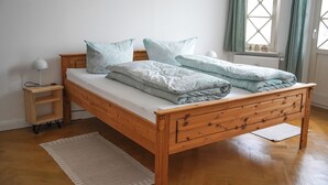 A wooden bed with a white mattress, two pillows, a bedside table with a lamp, and a window with curtains. - Helle und Klare Fewo in Altstadtvilla (Quedlinburg)