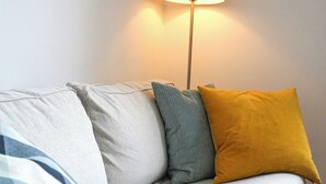 A grey sofa with multiple cushions, a floor lamp, and a wooden floor. - Helle und Klare Fewo in Altstadtvilla (Quedlinburg)