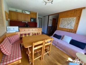 A compact living space with a kitchenette, a dining table, a sofa, and a wooden floor.