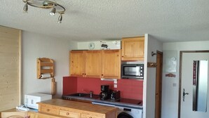 A compact kitchen with wooden cabinets, a microwave, a washing machine, and a dining area with a bench. - Comfortable apt. for 6 on ski slopes in Morillon (Morillon 1100)