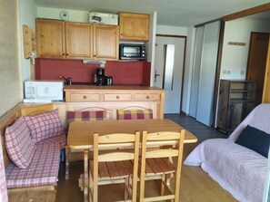 A compact living space with a kitchenette, a dining area with wooden furniture, and a sleeping area with a bed.