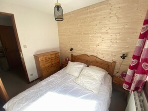 A bedroom with a wooden headboard, a wooden dresser, a bed with white bedding, and a hanging light fixture.