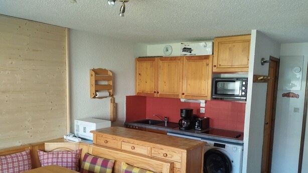 A compact kitchen with wooden cabinets, a microwave, a coffee maker, and a washing machine. - Comfortable apt. for 6 on ski slopes in Morillon (Morillon 1100)