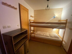 A bunk bed room with a wooden bunk bed, a small wooden shelf, and a hanging light fixture.