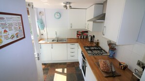 A kitchen with white cabinets, a wooden countertop, a gas stove, and a clock on the wall. - Delightful 2 bed garden cottage (free parking) (Brighton)
