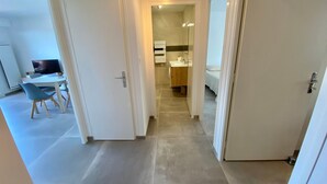 Un pasillo que conduce a un dormitorio con cama, un baño con lavamanos y un comedor con sillas y mesa.