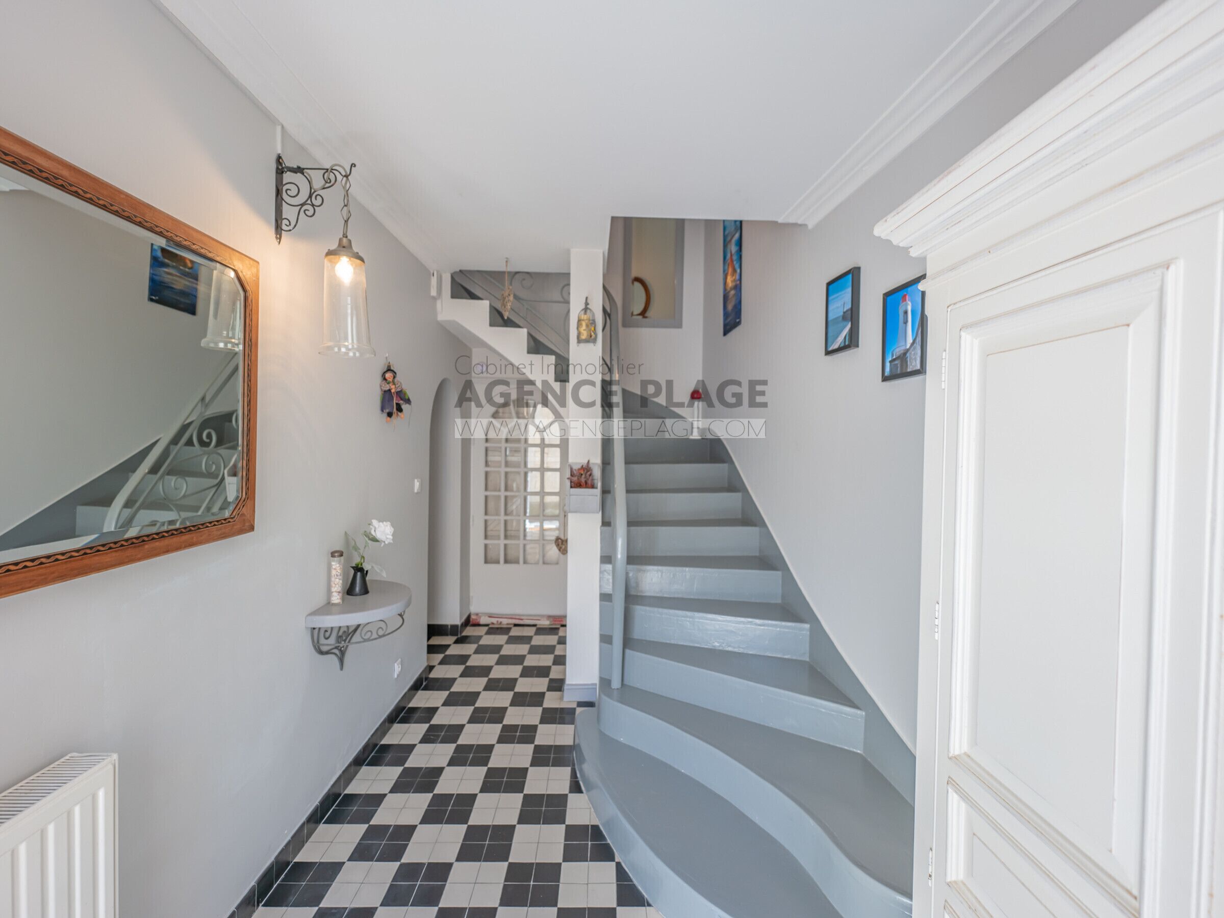 A hallway with a checkered floor, a white staircase, a mirror, a sink, and a radiator.