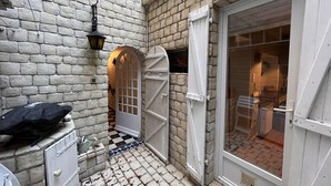 A narrow alleyway with a white door and a window, a checkered floor, and a lantern hanging on the wall.